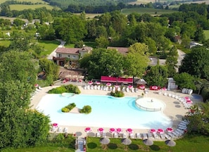 Ett flygbildsfoto av ett semesterområde med en stor swimmingpool, solstolar och en byggnad med rött tak.
