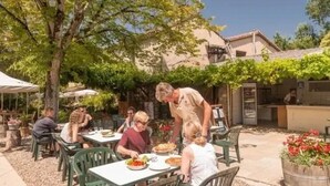 Ein Außenbereich zum Essen mit Tischen und Stühlen, eine Person bedient Essen, und im Hintergrund ein Gebäude.