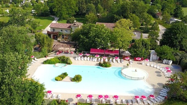 Ett flygbildsfoto av ett semesterområde med en stor swimmingpool, solstolar och en byggnad med rött tak.
