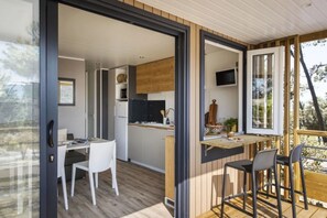Eine moderne Küche mit Holzausstattung, ein Essbereich mit weißen Stühlen und ein Balkon mit Holzterrasse.