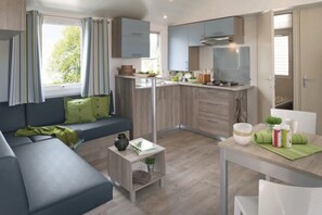 A modern kitchen with a dining area, a sofa, and a small table with a plant. - Camping 4 étoiles - Parc aquatique - ccbfhed (La Romieu)