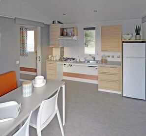 Eine moderne Küche mit weißen Schränken, einem Gasherd und einem Kühlschrank. Es gibt eine Essecke mit weißen Stühlen und einem Tisch.