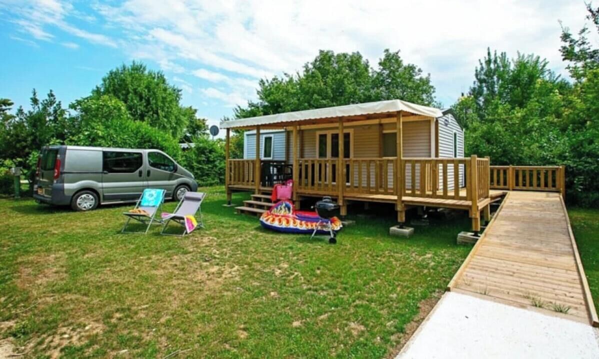 Una cabaña de madera con terraza, una camioneta y un set de parrilla instalados sobre el césped.