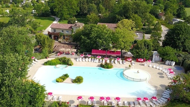 Ett flygbildsfoto av ett semesterområde med en stor swimmingpool, solstolar och en byggnad med rött tak.