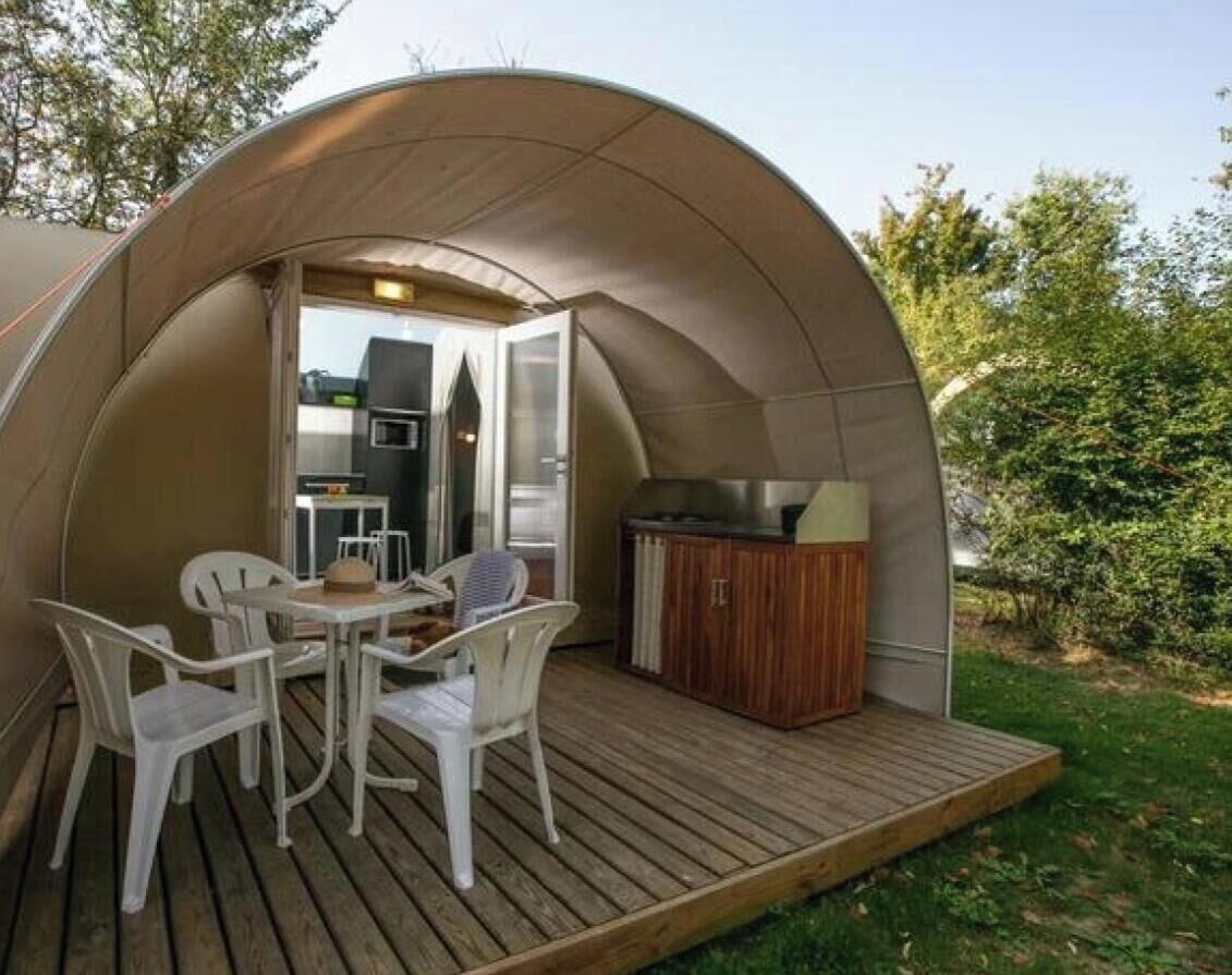 A dome-shaped tent with a wooden deck, a table with chairs, and a wood-burning stove.