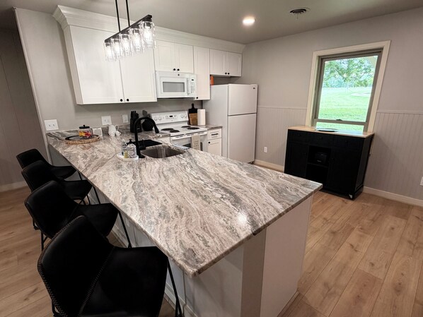 A kitchen with white cabinets, a marble countertop, a black refrigerator, and a window with a view of greenery.