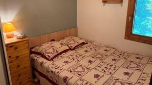 Una camera da letto con una testiera in legno, un comodino con una lampada, una coperta trapuntata e una finestra vista alberi.
