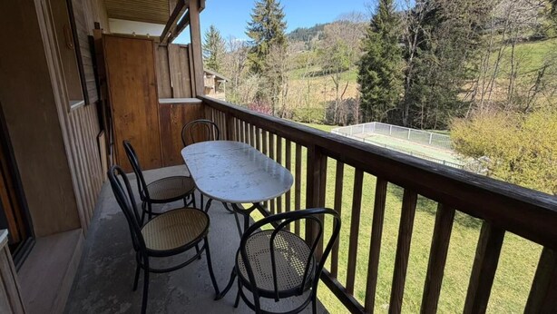 Un balcone con tavolo e sedie, affacciato su una zona verde e alberi.