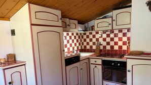 Una cucina compatta con mobili bianchi, uno schienale a scacchi rossi e bianchi e un soffitto in legno.