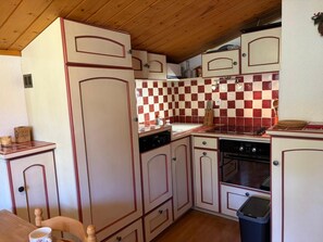 Eine kleine Küche mit weißen Schränken, einer roten und weißen Karosfliese und einer Holzbalkendecke.