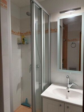 Ein Badezimmer mit einer gläsernen Duschkabine, einem weißen Waschbecken und einem Spiegel darüber.