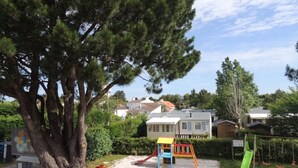 A playground with a slide and swings, surrounded by houses and a large tree. - Camping 3 étoiles - Piscine  - ccbfiec (Les Moutiers-en-Retz)