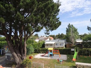 Un parque infantil con un tobogán y columpios, rodeado de casas y un árbol grande.
