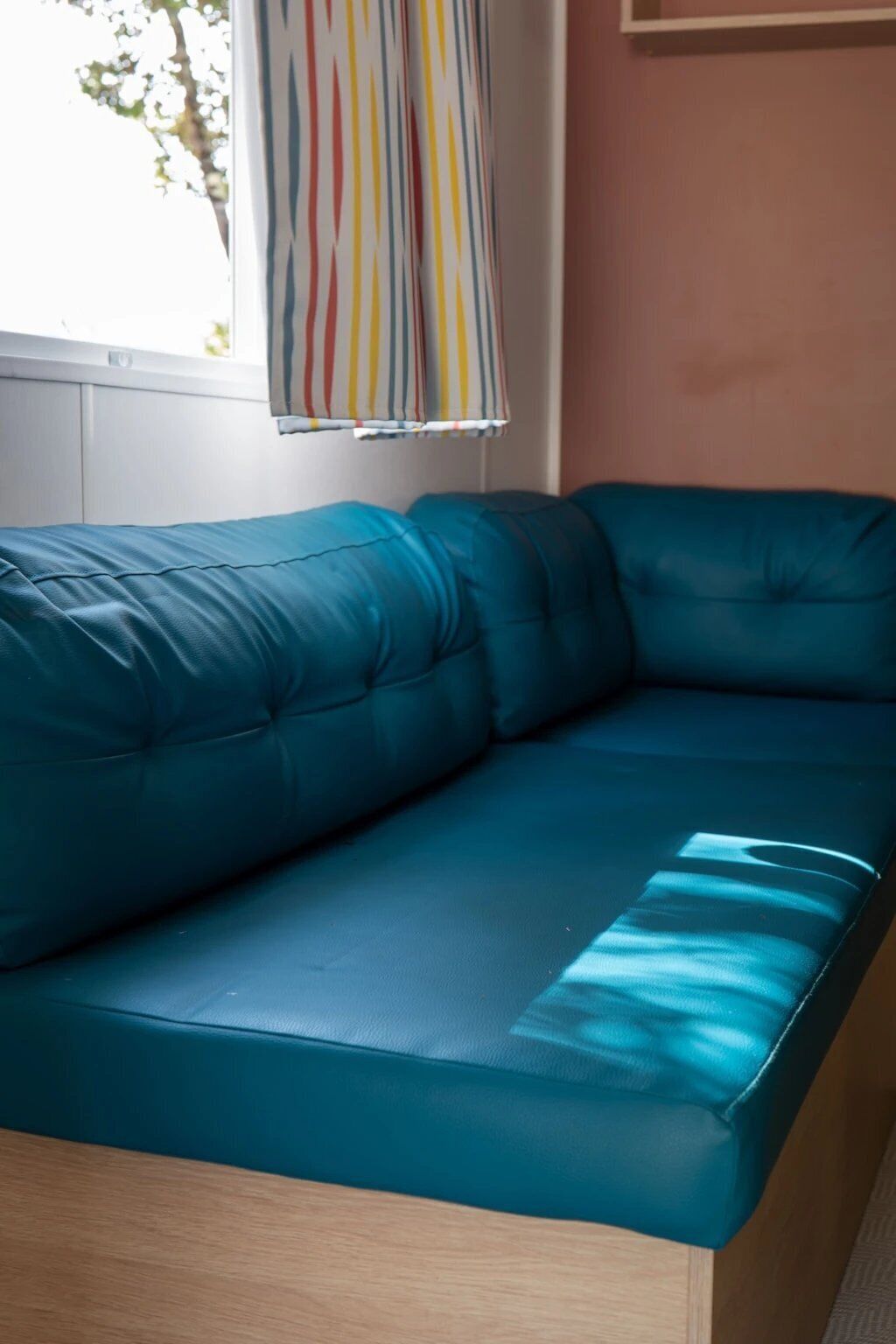 Een teal kleurige bank in een kamer met een raam, een gestreept gordijn en een houten vloer.