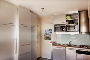 Eine kompakte Küche mit Kühlschrank, Mikrowelle und eingebautem Backofen.