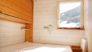 Ein Zimmer in einer Holzhütte mit einem Bett, einem Fenster mit Blick auf eine verschneite Landschaft und einem Holzregal.
