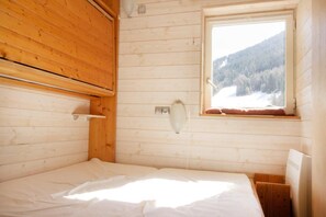 Ein Zimmer in einer Holzhütte mit einem Bett, einem Fenster mit Blick auf eine verschneite Landschaft und einem Holzregal.