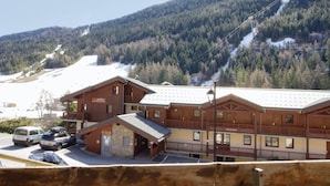 Ein Holzhaus mit Balkon, einem Schild mit der Aufschrift 'Hotel' und einer Skipiste im Hintergrund.