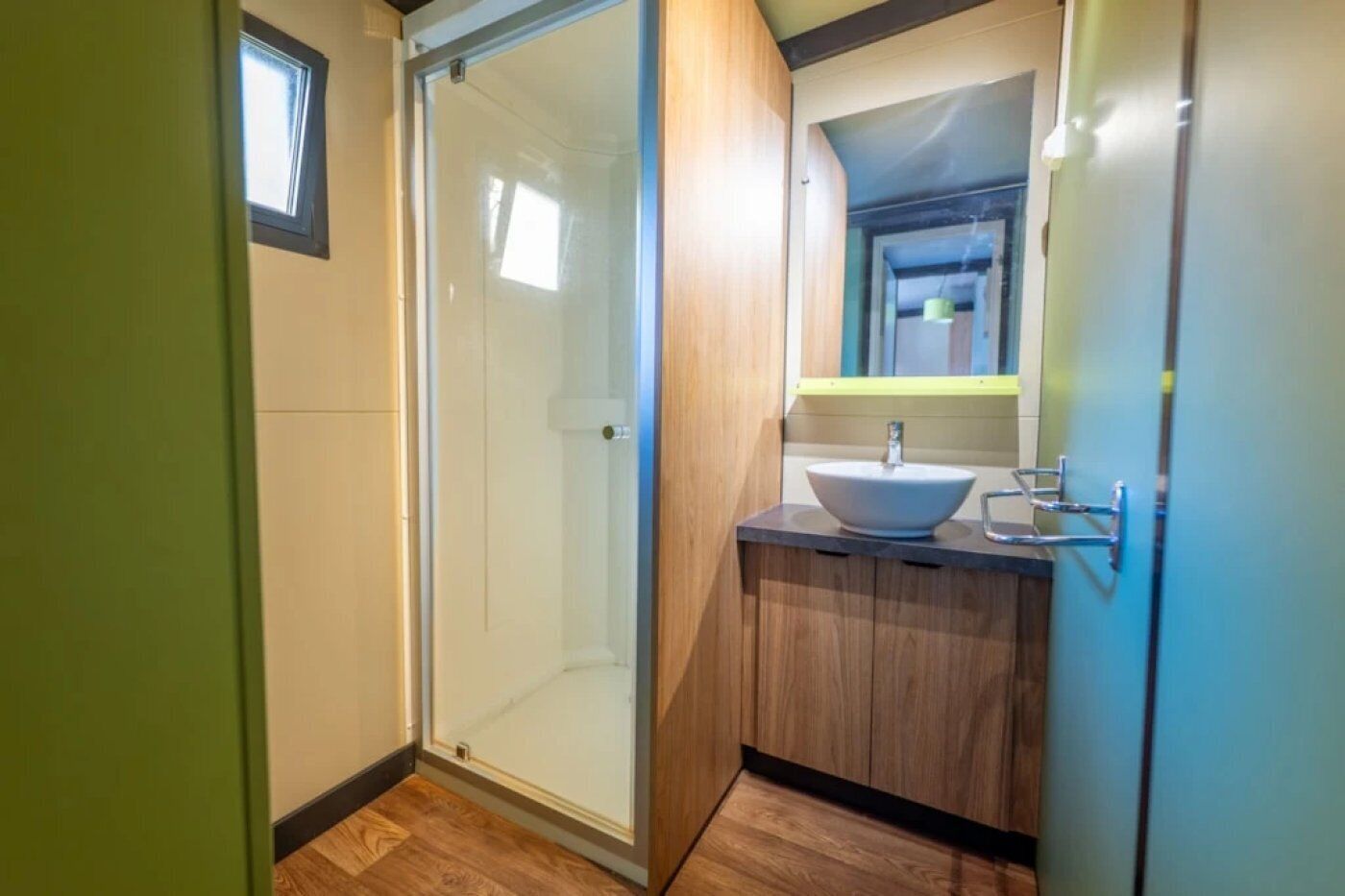 Une salle de bain avec une porte de douche en verre, un meuble-lavabo en bois et un lavabo.