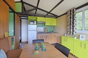 Eine kompakte Küche mit Mikrowelle, Kühlschrank und Spüle. Ein Esstisch mit Stühlen sowie ein grünes Schranksystem sind vorhanden.