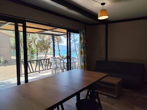 A room with a wooden table, a sofa, and a view through large windows.