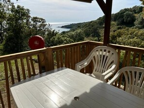 Une terrasse en bois avec une table et des chaises, offrant une vue panoramique sur la côte et les collines environnantes.