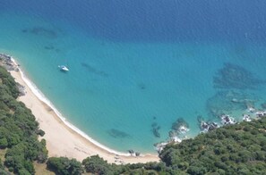 Vue aérienne d’une plage aux eaux turquoise et limpides, bordée d’un rivage sablonneux et d’une végétation verdoyante et luxuriante.