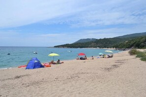 Ein Strand mit Zelt, Sonnenschirmen und entspannten Menschen.