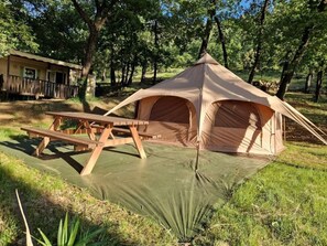 Ein Zelt mit Picknicktisch auf einer grünen Plane in einem Waldgebiet.