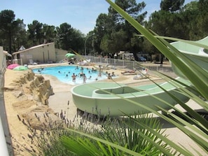 Uma área de piscina com um toboágua, rodeada por uma praia de areia e vegetação.