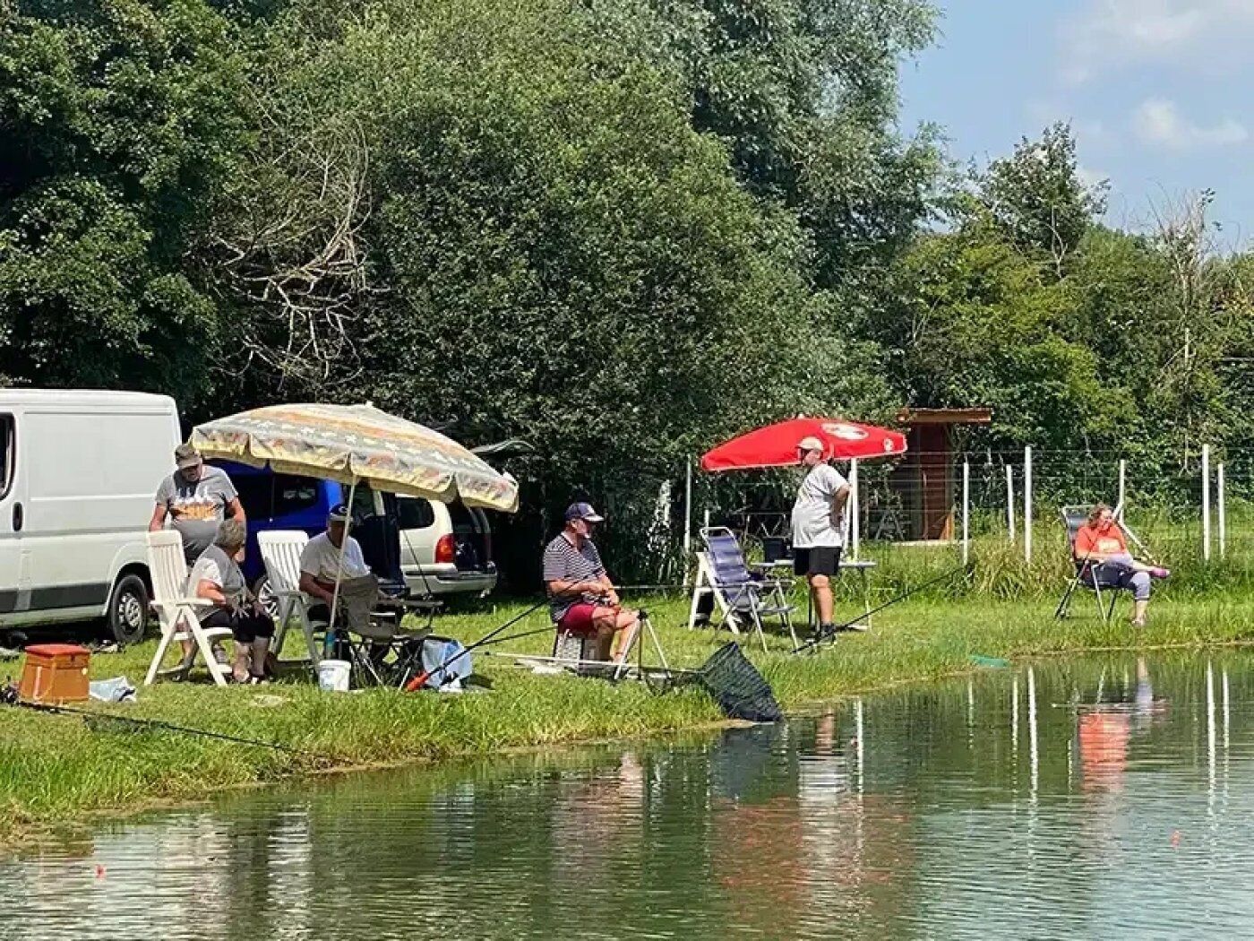 A lakeside setting with people fishing, a white van, and a red umbrella.