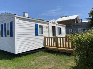 A white mobile home with blue shutters, a wooden deck, and a small porch. - Camping 3 étoiles - Piscine  - ccbfhic (Rue)