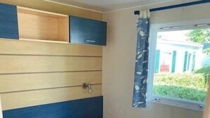 Une petite chambre à coucher comprenant un lit, une table de chevet, une fenêtre avec des rideaux et une étagère intégrée au-dessus du lit.