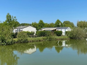 A lakeside property with two white buildings, one with a porch and another with a covered patio. - Camping 3 étoiles - Piscine  - ccbfhie (Rue)