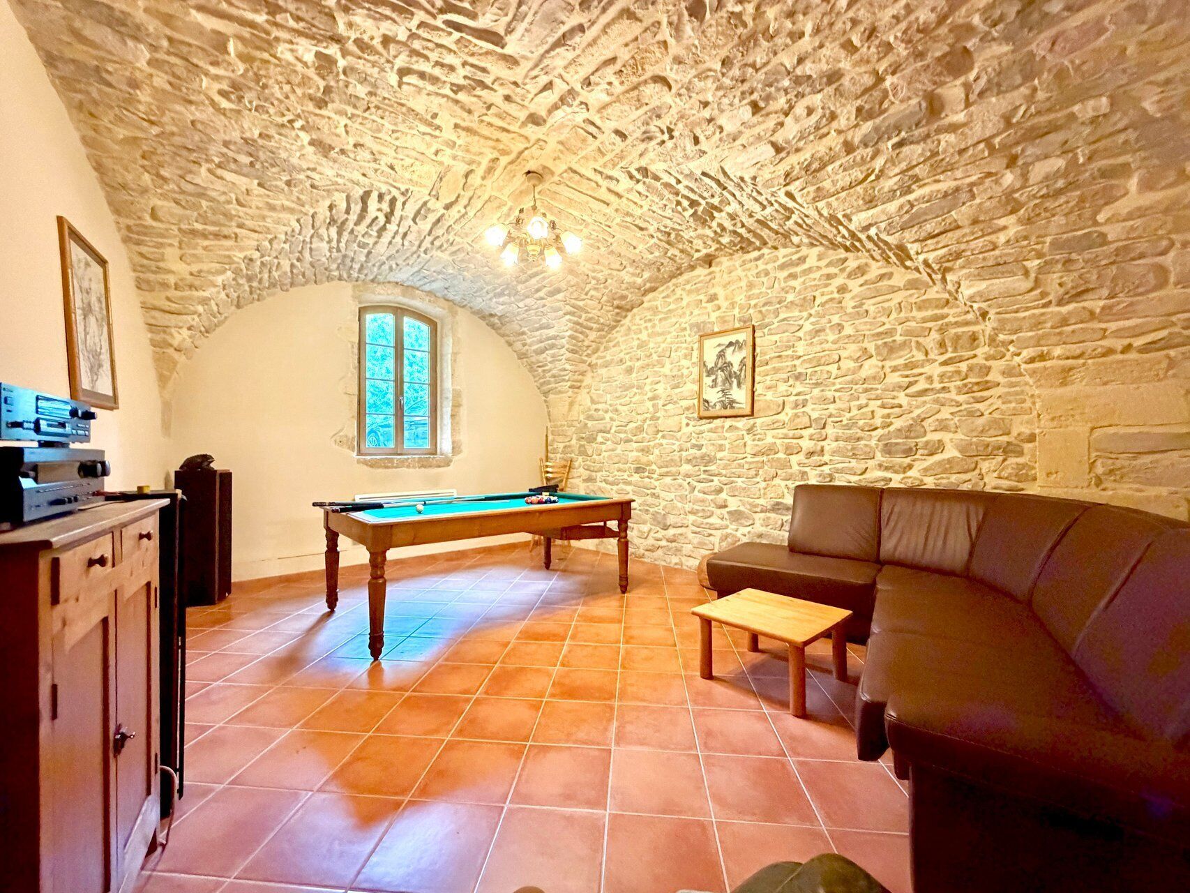 A room with a pool table, a sofa, a small table, and a stone ceiling.