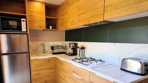 Una cocina compacta con armarios de madera, un microondas integrado, un refrigerador de acero inoxidable, una estufa a gas y un tostador.