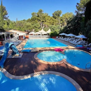 Ein Poolbereich mit mehreren Schwimmbecken, Liegestühlen und Sonnenschirmen.