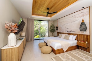 Ein modernes Schlafzimmer mit einem großen Bett, Deckenventilator, Holz-Kopfteil, Nachttisch, einer Vase mit Blumen, einem Fenster mit Vorhängen und Blick auf Grünfläche.