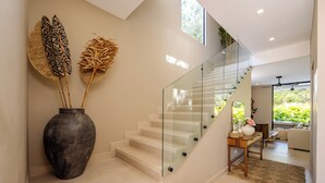 Un escalier moderne avec des rampes en verre, un vase orné de feuilles décoratives et une vue sur un espace de vie comprenant un canapé et une table basse.