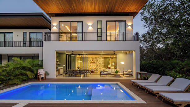 Une maison moderne à deux étages dotée d’une piscine, d’un espace salon extérieur et d’un balcon.