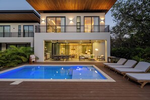 Une maison moderne à deux étages dotée d’une piscine, d’un espace salon extérieur et d’un balcon.
