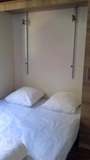 Un lit simple avec une literie blanche, dans une pièce dont le plafond est en bois et un des murs est blanc.