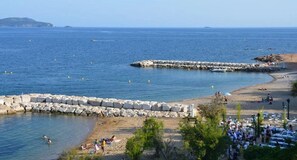 Une plage côtière avec une digue rocheuse, une mer bleue et limpide, et des gens qui profitent des lieux.