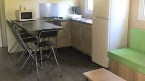 Uma cozinha compacta com micro-ondas, fogão e geladeira. Há uma área de refeições com mesa e cadeiras.