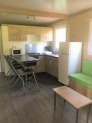 Une cuisine compacte équipée d’un four à micro-ondes, d’une cuisinière et d’un réfrigérateur. Un coin repas avec une table et des chaises est également disponible.