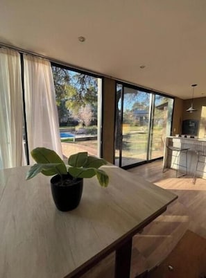 Una cocina moderna con ventanas amplias, una mesa de comedor con una planta en maceta y una escalera que sube a un nivel superior.
