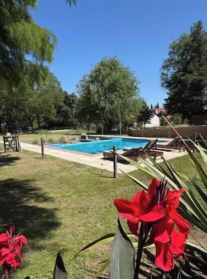 Piscina con sillas de descanso, rodeada de césped y árboles.