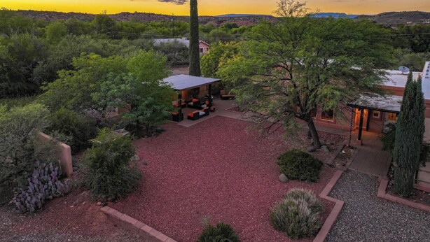 A courtyard with a covered seating area, surrounded by trees and shrubs, with a view of distant hills.