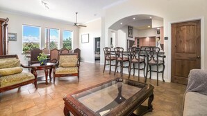 A spacious living room with a large glass coffee table, a dining area with wooden chairs, and a kitchen visible through an archway.