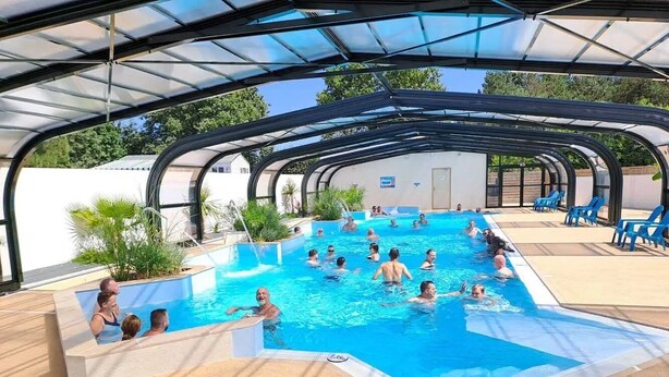 A covered swimming pool with people swimming and lounging, surrounded by a patio area with chairs.